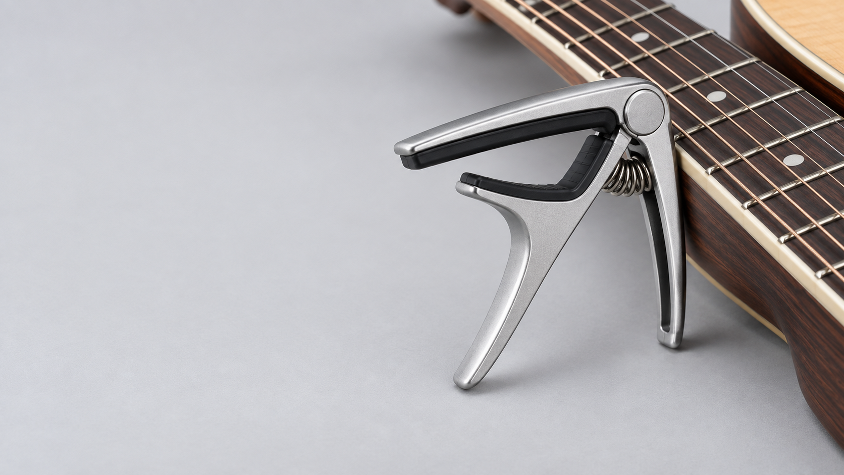 Unbranded metal guitar capo beside an acoustic guitar neck